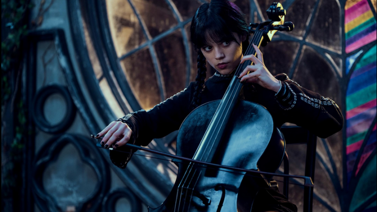 Jenna Ortega as Wednesday seated and playing a cello in her spooky dorm room